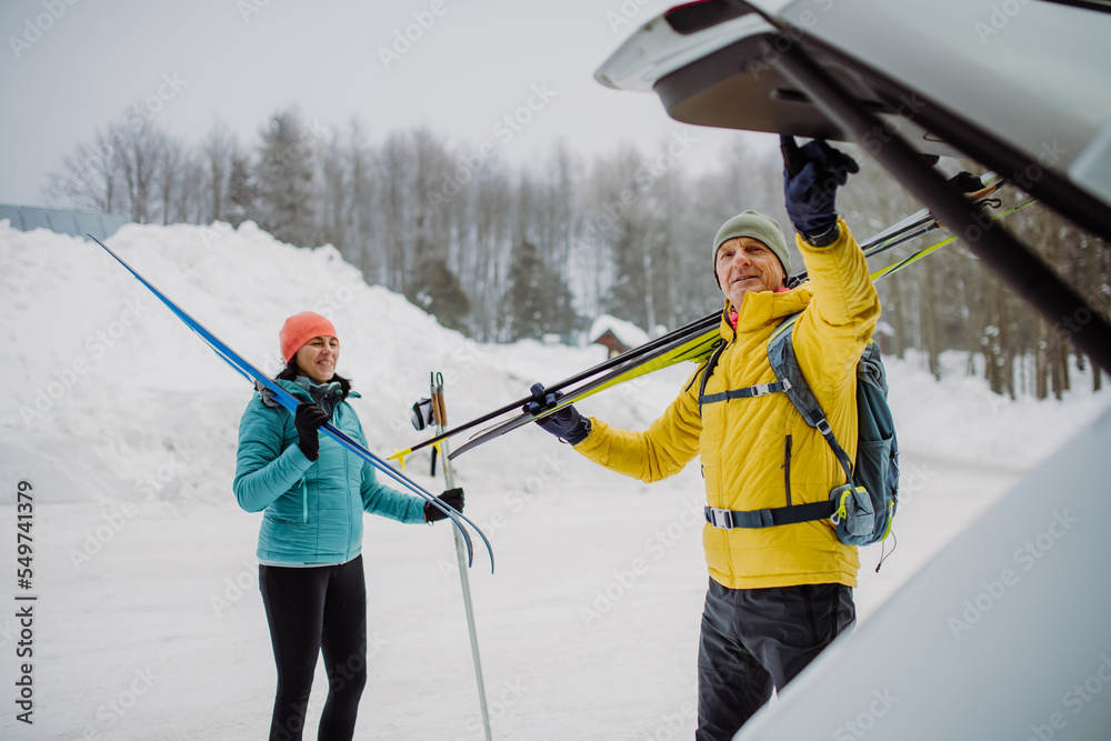 Senior couple near car trunk preparing for winter skiing.
